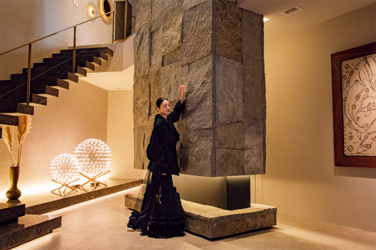 リゾートハウスYUNI 大島石のオブジェウォールの前に立つ松雪 泰子さん